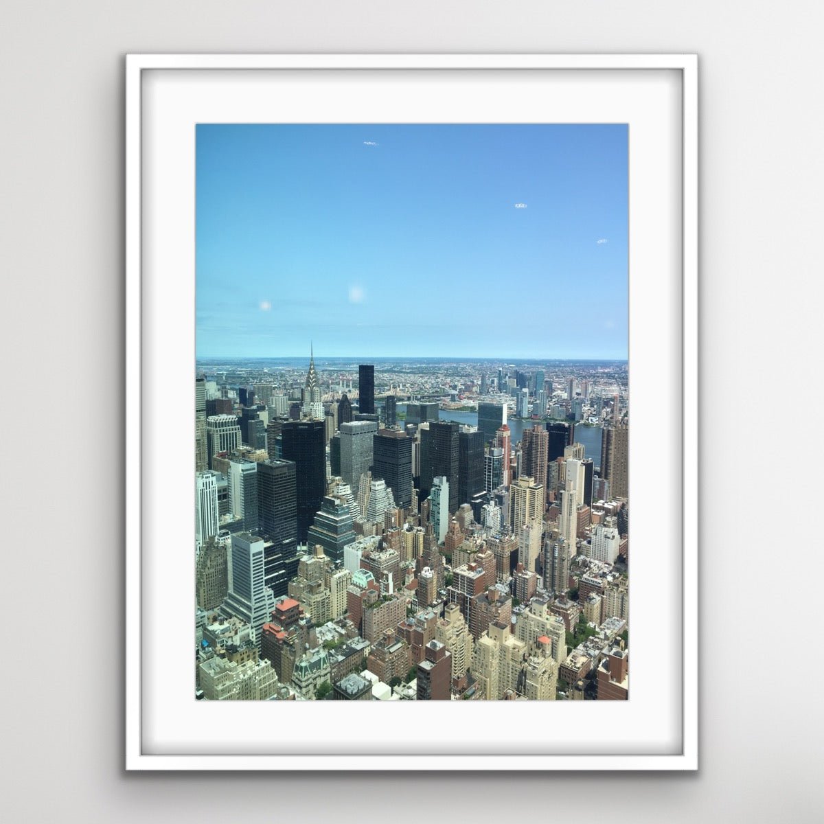 Eingerahmtes Foto der Skyline von New York City mit zahlreichen Wolkenkratzern unter klarem, blauem Himmel – ein Panorama der Stadtlandschaft.