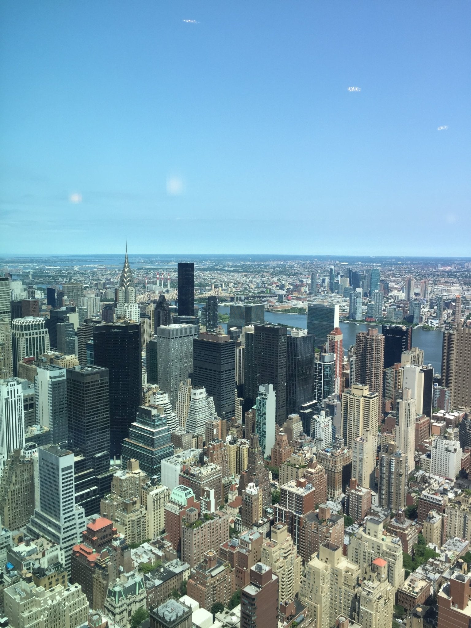 Blick auf die Skyline von New York City mit markanten Wolkenkratzern, darunter das Chrysler Building, unter klarem, blauem Himmel.